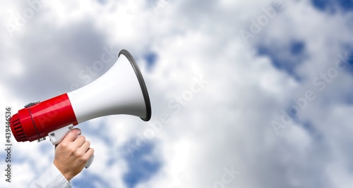 A hand holds a megaphone. The Horn loudspeaker. Clouds background. The concept of a message.