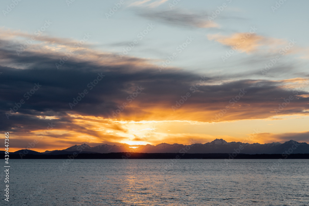 Cloudy and dramatic sunset over the bay and the Cascade mountain range in Seattle, Washington Cloudy and dramatic sunset over the bay and the Cascade mountain range in Seattle, Washington