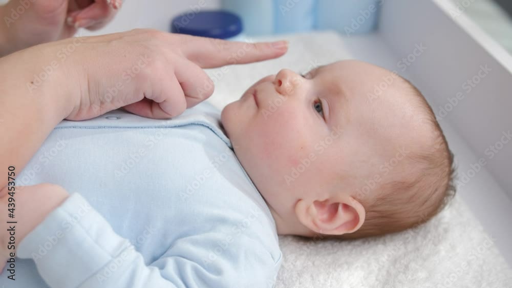 Cute little baby boy lying on dressing table while mother applying moisturizing and cleaning creme. Concept of hygiene, baby care and healthcare Cute little baby boy lying on dressing table while mother applying moisturizing and cleaning creme. Concept of hygiene, baby care and healthcare