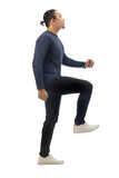 Man wearing casual blue shirt black denim and white shoes, looking up forward and stepping high, side view climbing stair gesture. Full body portrait isolated