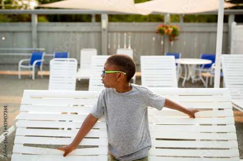 Boy leans on deck chairs and looks off into distance