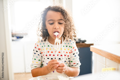Curly haired girl licking frosting off a beater