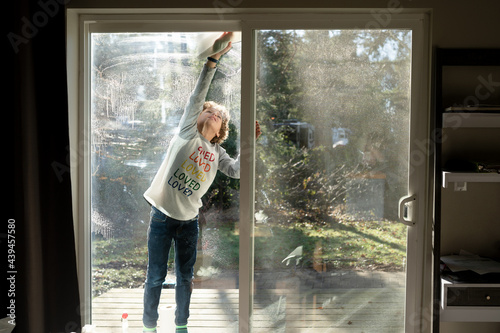 Cute boy stands on porch cleaning sliding glass door
