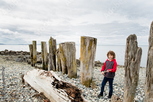 Boy stands by rotting driftwood pilings on rocky coastline 