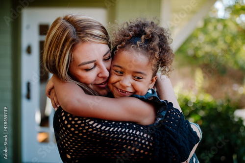 Loving mom embraces smiling biracial daughter on porch of house photo
