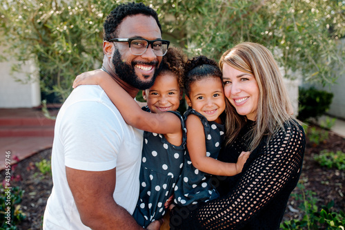 Happy parents holding adorable biracial daughters in matching outfits photo