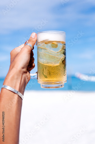 Crop woman with glass of beer on beach