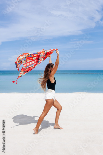 Carefree woman running along beach with fluttering scarf