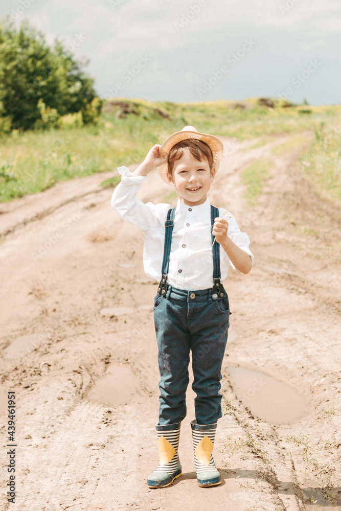 Little farmer on a summer field, cute little boy in a straw hat. boy in a hat with a flower stands in a field. portrait of a village boy Little farmer on a summer field, cute little boy in a straw hat. boy in a hat with a flower stands in a field. portrait of a village boy