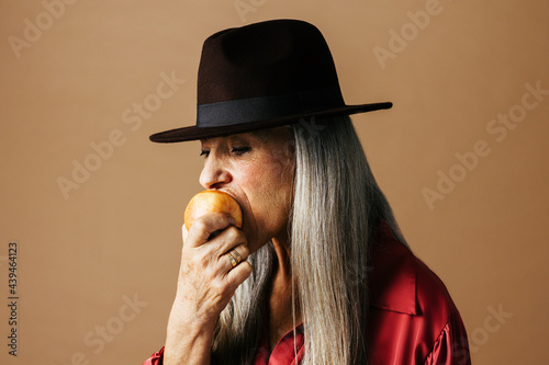 Elegant aged woman in hat biting apple photo