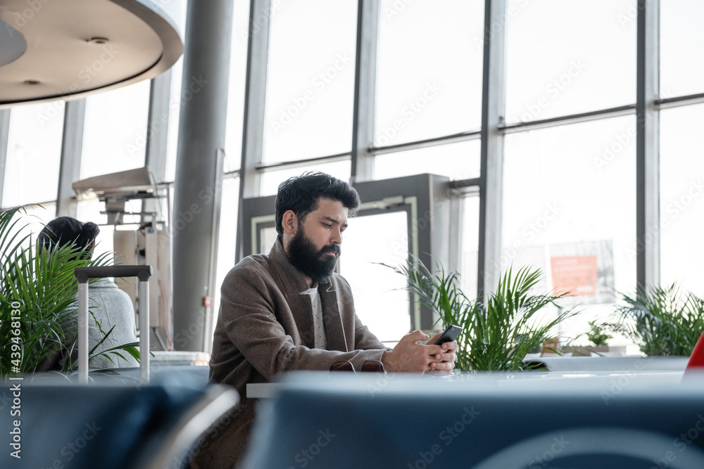 Bearded traveler using smartphone in airport waiting room Bearded traveler using smartphone in airport waiting room
