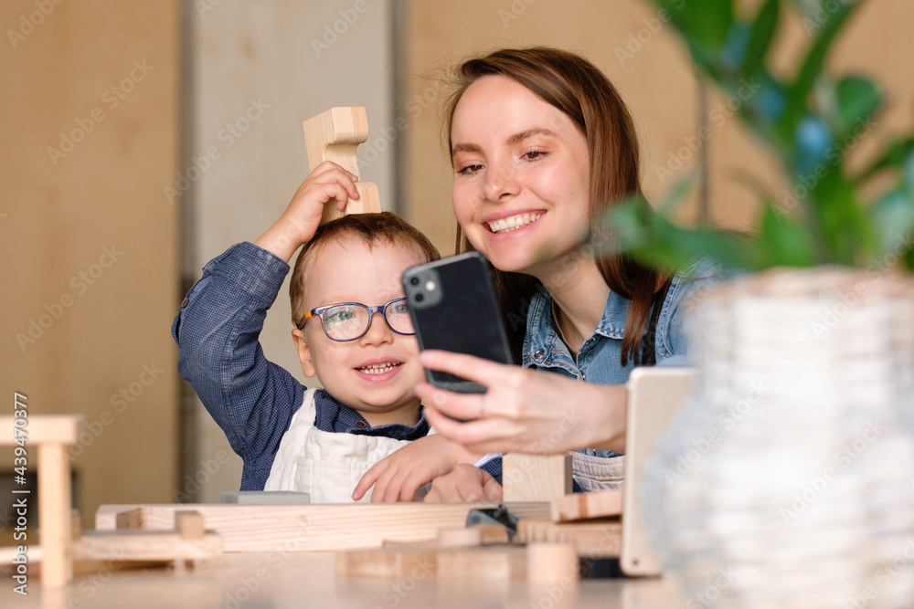 Happy mother and funny kid taking selfie while making wooden toy together Happy mother and funny kid taking selfie while making wooden toy together
