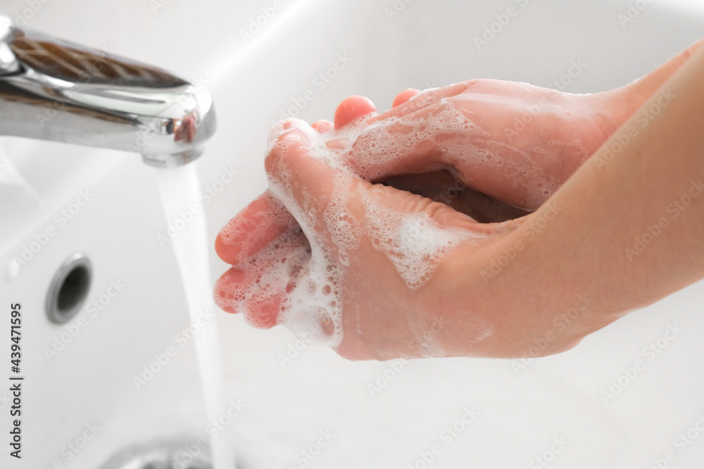 Fototapeta premium Hands of woman wash their hands in a sink with foam to wash the skin and water flows through the hands. Concept of health, cleaning and preventing germs and coronavirus from contacting hands