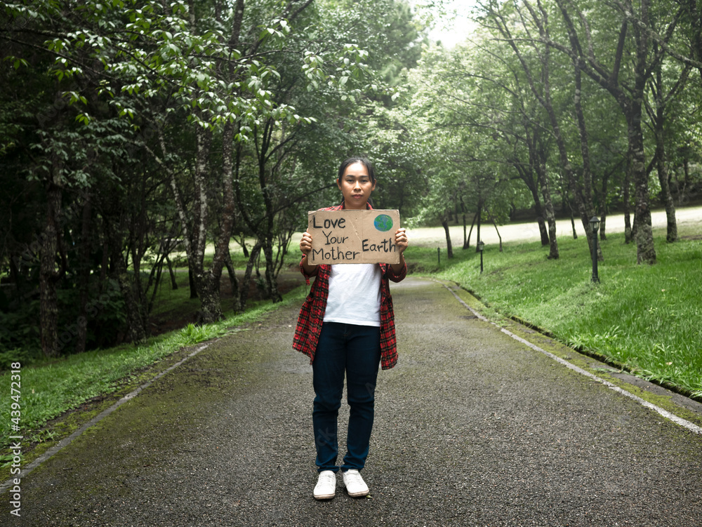 A female volunteer holding a nature conservation sign stands among the nature in the forest. The concept of World Environment Day.
