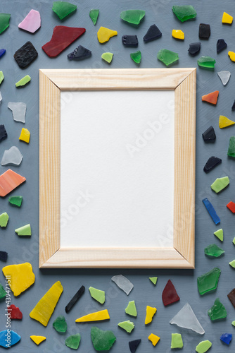 Stationery mock-up scene. Blank white greeting card in wooden frame surrounded by pieces of colorful sea glass on textured gray background.
