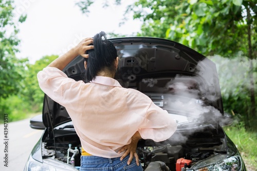 Asian woman having problem with broken, overheat car while driving alone on the road standing with smoke from the engine photo