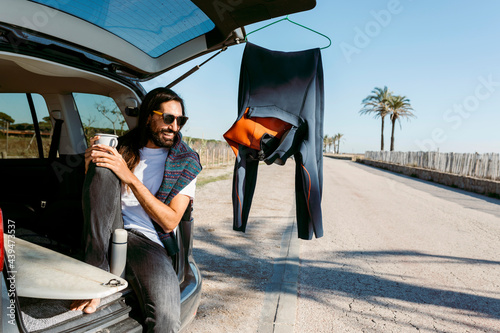 man with hot beverage sitting on car trunk photo