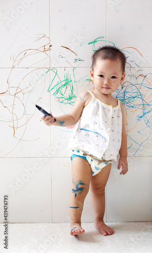 Cute Asian kid painting casually on the wall at home photo