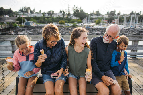 Grandparents and grandkids laugh and sit on a bench on a dock wh photo