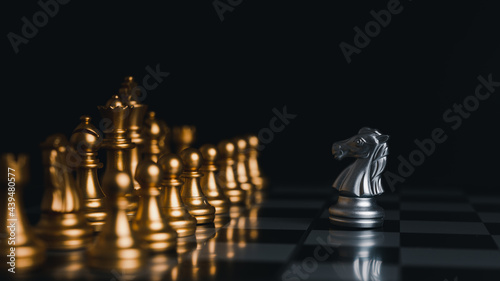 The silver horse in the chess board game is facing another golde team. Competition,Strategic ideas for business wins. on black background.