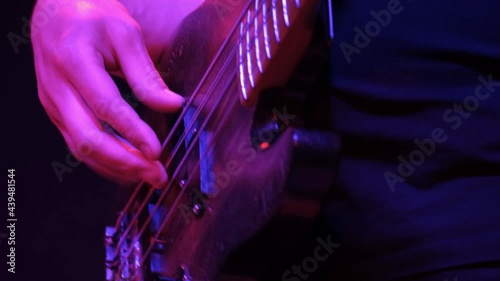 Male guitarist playing electric bass guitar on a rock concert in a club. Red lighting, hands closeup.