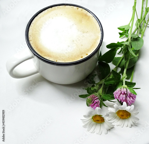 Cup of fresh coffee with milk foam and wild flowers on white background, top view