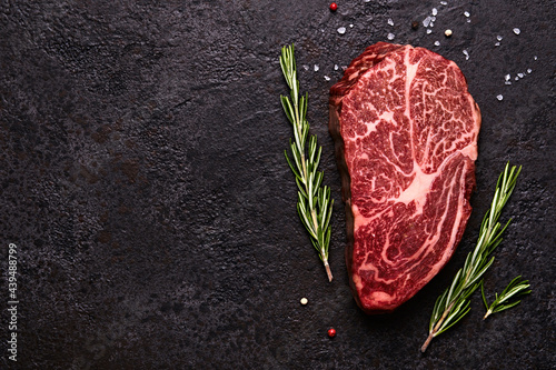 Fresh raw marbled beef rib eye steak and spices on black stone background, copy space photo