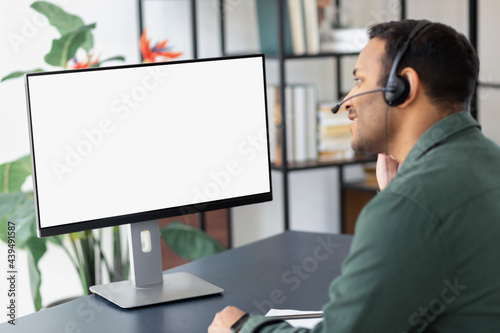Happy indian businessman in headset looking at blank computer screen, studying at home concept distance education, online meeting, video call