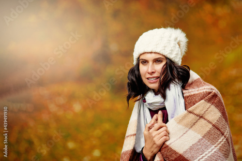 Beautiful young brunette woman in warm plaid having walk in autumn park