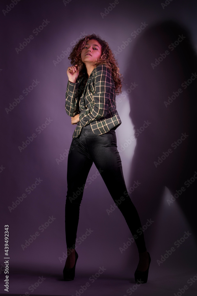 vertical portrait of a curly model wearing a jacket, black pants and high heel shoes in a purple backgroung vertical portrait of a curly model wearing a jacket, black pants and high heel shoes in a purple backgroung