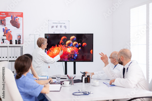 Virolog senior woman discussing about coronavirus symptoms during meeting in conference room. Physician teamwork explaining medical vaccine against global pandemic monitoring virus risk photo