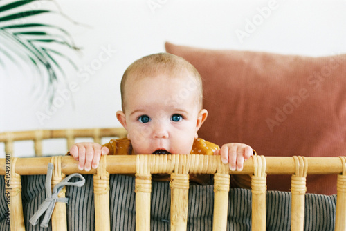Baby girl teething on rattan baby bed photo