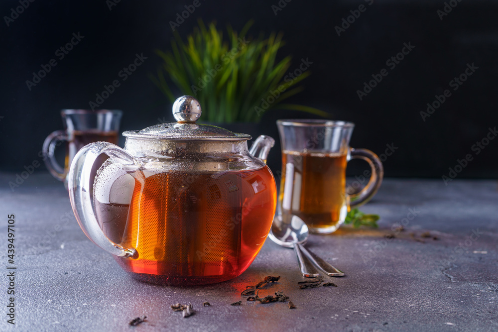 Black tea in a clear glass teapot on a dark background. Black tea in a clear glass teapot on a dark background.