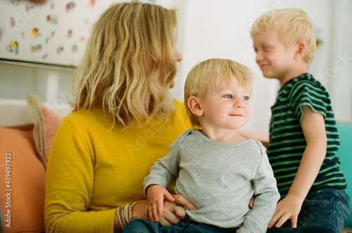 Cute young blond-haired boy on mother's lap indoors with old brother nearby photo