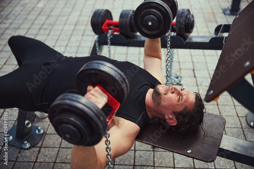 Kind bearded male person lifting heavy dumbbells