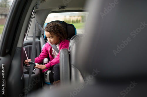 Girl in back seat of van writes with pencil