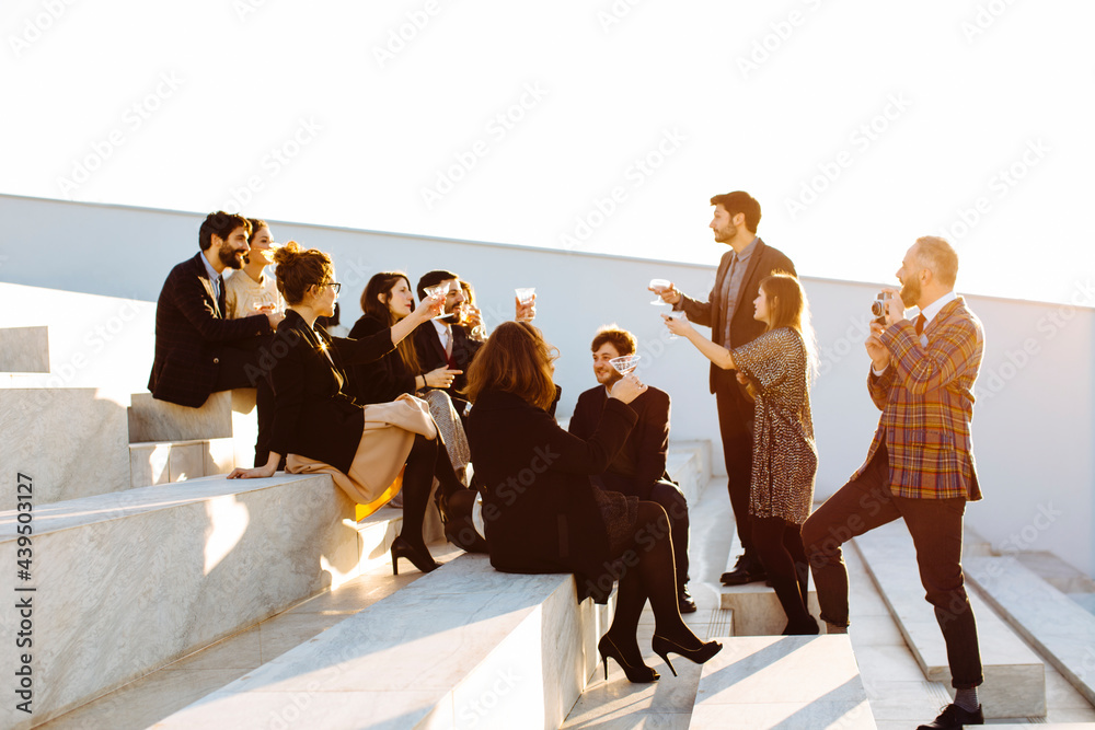 © sofie delauw/Stocksy - Stylish colleagues with wine celebrating festive occasion on stairs