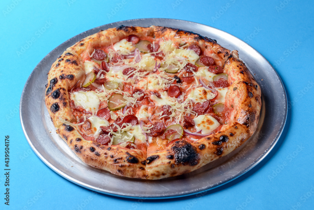Pizza with bavarian sausages, Mozzarella cheese, onion and cucumbers isolated on blue background. Pizza with bavarian sausages, Mozzarella cheese, onion and cucumbers isolated on blue background.