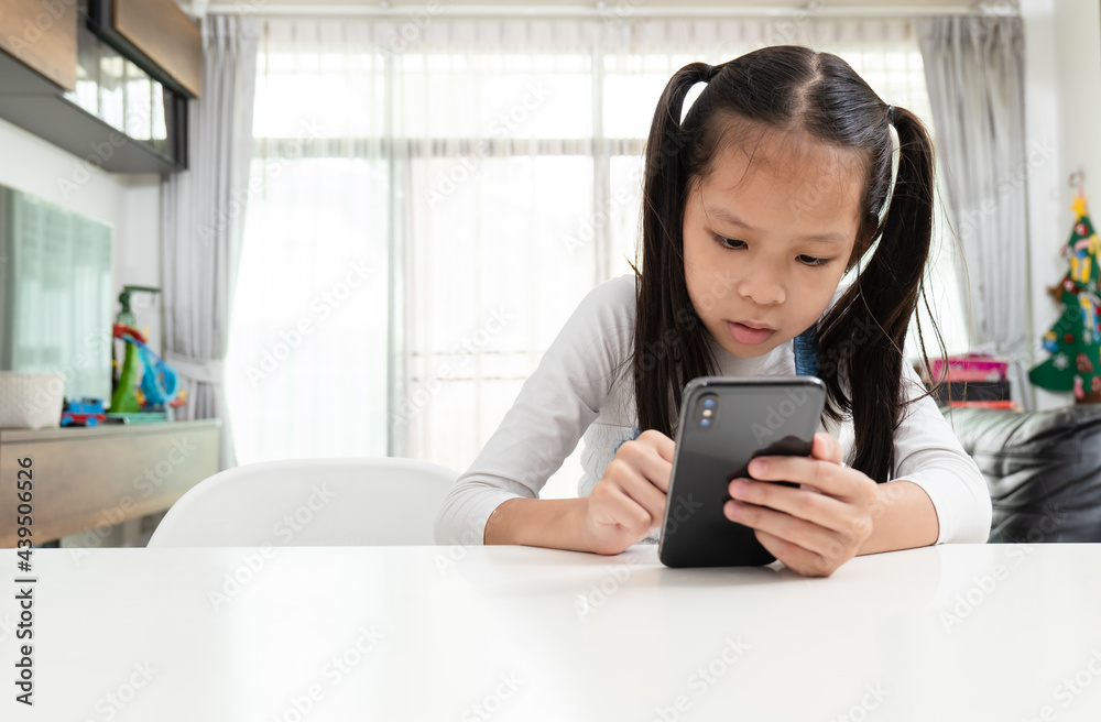 Asian girl with white t-shirt sitting to table browsing smartphone at home. Asian girl with white t-shirt sitting to table browsing smartphone at home.