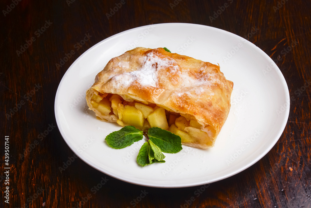 Slice of delicious fresh baked Rustic Apple Pie served on a white plate on wooden table background.