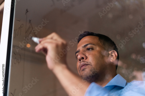 Latin hispanic man working at home and writting graphs on glass wall