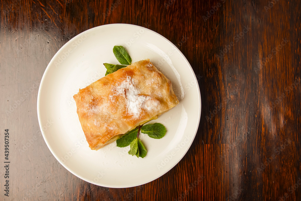 Slice of delicious fresh baked Rustic Apple Pie served on a white plate on wooden table background.