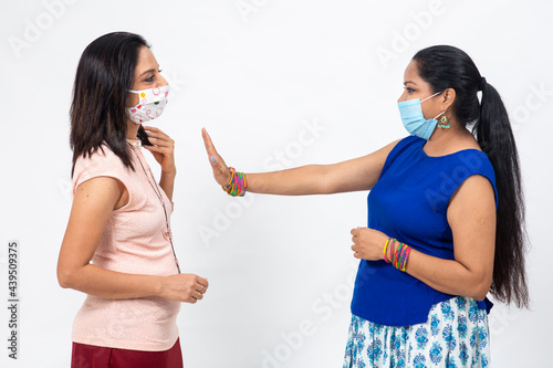Two pretty Indian women wearing Covid-19 protection mask. Two females indicate social distancing between themselves.