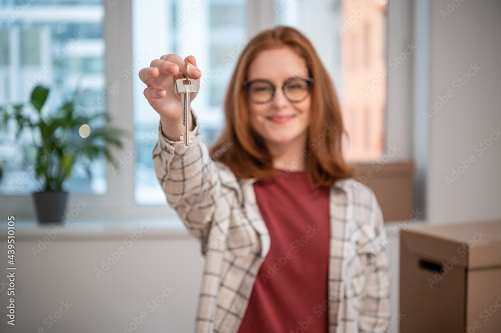 Portrait of a young girl with glasses, she shows the camera the keys to her new apartment