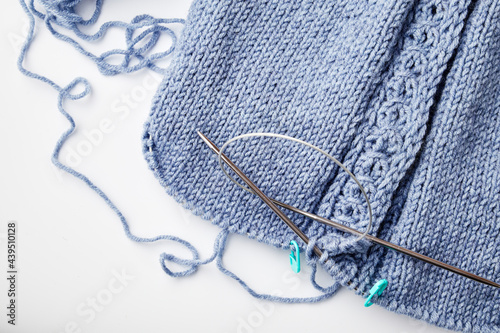 blue knitted product on knitting needles on a white background