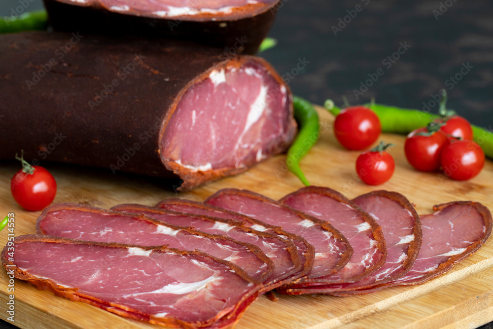 Turkish pastrami on a wooden serving plate. Whole and sliced pastrami