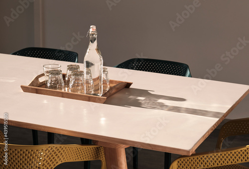 Water bottles and glasses with water on a clean and tidy table in the afternoon sun