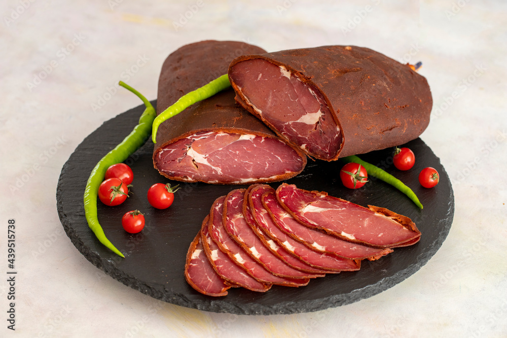 Turkish pastrami on a black stone serving plate. Whole and sliced pastrami. Pastrami is made