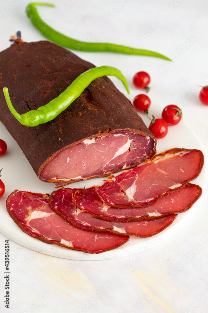 Turkish pastrami on a white marble background. Whole and sliced