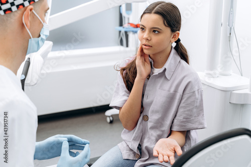 Girl touches her cheeks with her hand. A cute, crooked girl tells the dentist that she has a toothache.